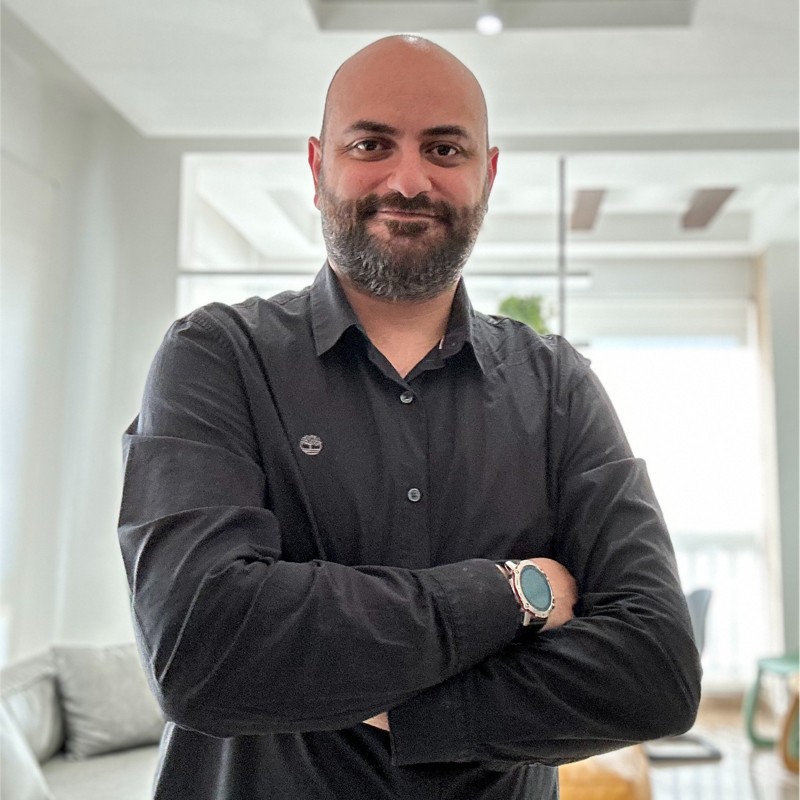 Portrait of Fady Abboud, standing with arms crossed in a bright room, wearing a dark shirt.